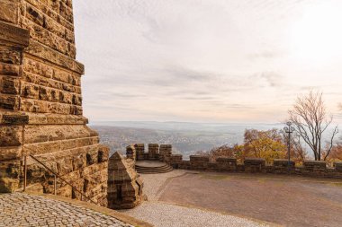 Büyük Wilhelm anıtından Almanya 'nın Port Westphalia kentinin manzarası. Ufukta bulutlu bir gökyüzü, akşam ve puslu tepeler var. Resim anıtın duvarlarını gösteriyor..