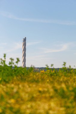 Uzakta, üzerinde açık mavi bir gökyüzü olan uzun bir test kulesi var. Kule uzun otlarla çevrili ve gökyüzü bulutlarla dolu. Huzurlu ve huzurlu bir sahne..