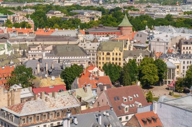 Riga, Letonya 'nın bir kısmının panoramik fotoğrafı. Fotoğraf açık havada çekilmişti. Gökyüzü mavi. Yuvarlak kırmızı tuğla bir kule ve kedili sarı bir ev görebilirsiniz..