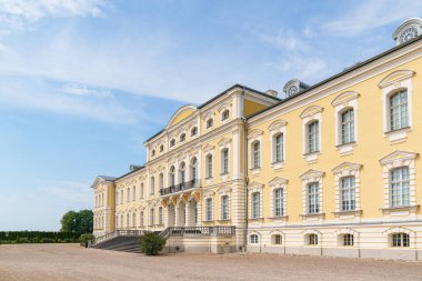 Letonya 'daki büyük sarı Rundale sarayı açık mavi gökyüzünün altında duruyor. Simetrik pencereler zarif taş cephe hattında. Geniş merdiven büyük giriş basamaklarına çıkar..