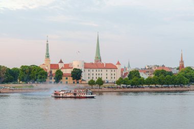 Riga, Letonya 'daki Dune Nehri boyunca Riga Palace' ın arka planında bir gezi gemisi hareket eder. Fotoğraf alacakaranlıkta çekildi..