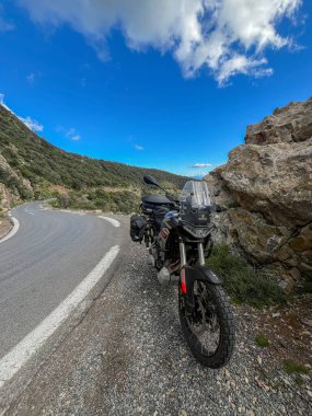 Djurdjura dağlarında büyük bir kaya oluşumunun yanındaki dolambaçlı bir dağ yolunda park etmiş motosiklet macerası..