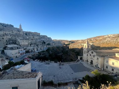 Antik Sassi di Matera şehrinin geniş panoramik manzarası ve açık mavi gökyüzünün altındaki taş bir kilise..