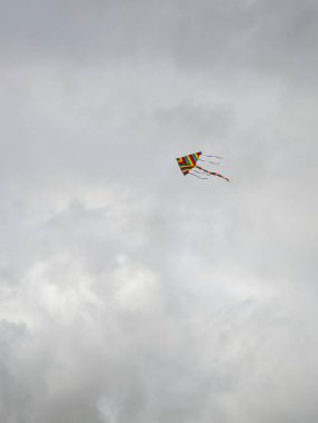 Gri bulutlu gökyüzünde uçan renkli gökkuşağı çizgili uçurtma.