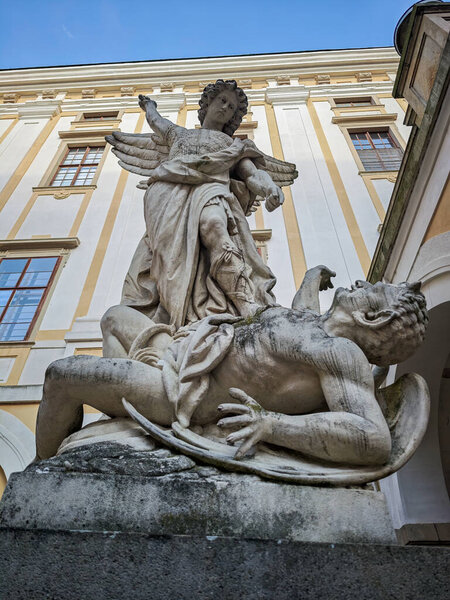 Baroque stone sculpture of Archangel Michael defeating a demon in a castle garden.
