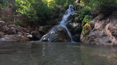 Cascading natural waterfall, clear water, rocky bottom, green trees, High quality photo