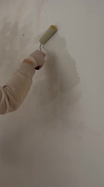 Duvarı boyayan kişi. Bir ressam silindirle beyaz bir duvar boyuyor. Yüksek kalite 4k görüntü