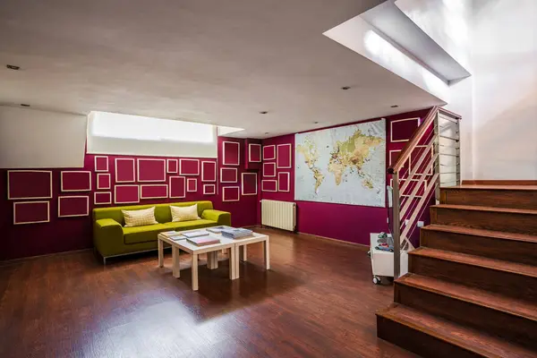 明るい緑のソファを備えた木製の床と階段を備えた現代的な広々としたリビングルームと赤い壁に幾何学的な要素が飾られています — ストック写真