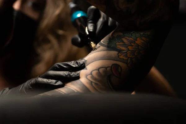 Kobieta Mistrz Tatuażu Masce Maszyną Tatuażu Ramieniu Męskiego Klienta Ciemnym — Zdjęcie stockowe