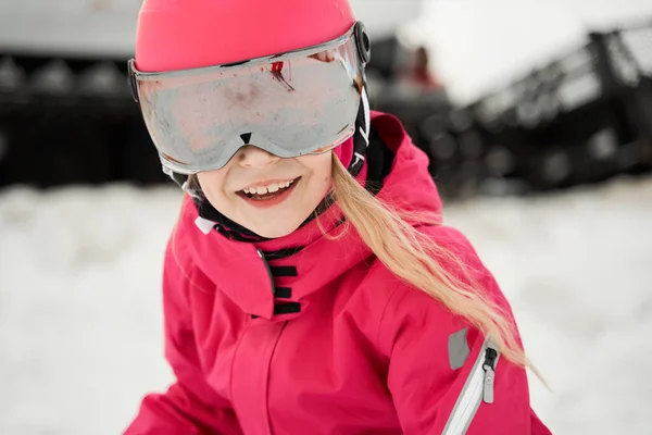 在晴朗的冬日 穿着粉色保暖活动服 戴着护目镜 头戴安全帽 沿着雪坡滑行的可爱女孩 — 图库照片