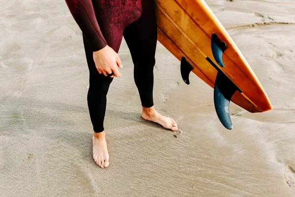 日出日落时穿着湿衣站在海滩上与冲浪板站在一起的无名小卒 — 图库照片
