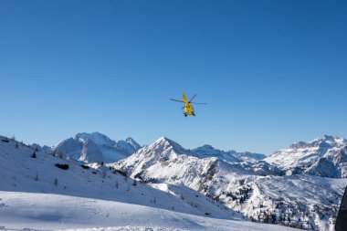 İtalya 'da karla kaplı Dolomitler üzerinde faaliyet gösteren sarı dağ kurtarma helikopteri dramatik kış manzarasına karşı Alp acil servislerini ön plana çıkarıyor.