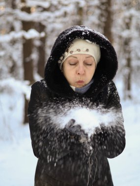 Siyah ceketli bir kadın avuçlarına kar üflüyor. Önplan.