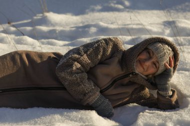 Karda uzanmış bir kadın, elleriyle başını kaldırıyor ve gülümsüyor..