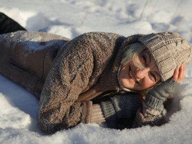 Gülümseyen bir kadın, dirseklerine yaslanarak karın üzerine uzanır. Önplan.