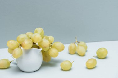 Gri arkaplanda beyaz bir sürahi içinde üzümler.