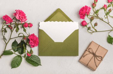 Kadınsı davet ya da boş ve yeşil zarflı tebrik kartı modeli, el işi hediye kutusu ve açık arkaplanda pembe güller.