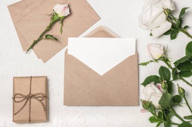 Düz davetiye ya da el işi zarflı tebrik kartı modeli, hediye kutusu ve açık arkaplanda beyaz güller..