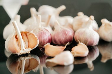 Taze sarımsak soğanları ve kabuğu soyulmuş karanfiller koyu yansıtıcı yüzeyde sağlıklı yemek malzemeleri ve doğal baharatlar.