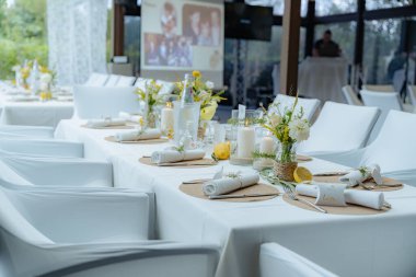 Düğün masası çiçeklerle ve mumlarla zarif bir şekilde ayarlanmış sofistike bir atmosfer yaratıyor. Plakalar ve çatal bıçak takımı düzgünce düzenlenmiş, kurulumun görsel çekiciliğini arttırır