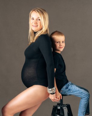 Hamile bir kadın oğluyla sırt sırta oturup aile bağını ve bağlantıyı sembolize ediyor. Stüdyo fotoğrafı