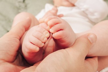 Aile sevgisi, şefkat ve doğal ışıkta korunma kavramında bebek ayakları tutan ebeveyn.