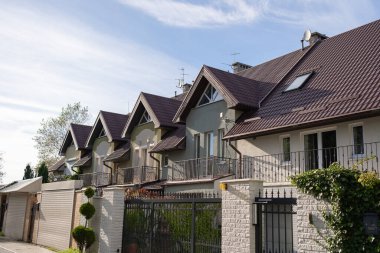 Row of modern private houses with pitched roofs, fenced yards and landscaped greenery. A quiet suburban neighborhood showing residential architecture and peaceful living