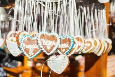 A row of small gingerbread hearts hangs neatly from white ribbons at a market stall. The soft sunlight highlights the icing borders and delicate handwritten patterns