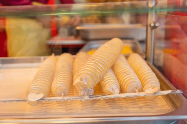 Raw spiral-cut potatoes coated in batter and arranged on sticks before deep-frying. The close-up highlights their textured surface and uniform shape, capturing a classic street-food preparation moment