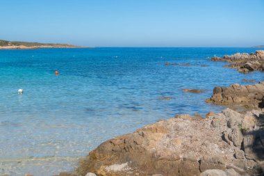 Turkuaz kıyı suları, parlak bir yaz gökyüzü altında engebeli kıyı kayalarıyla buluşur. Sardunya, La Maddalena, İtalya
