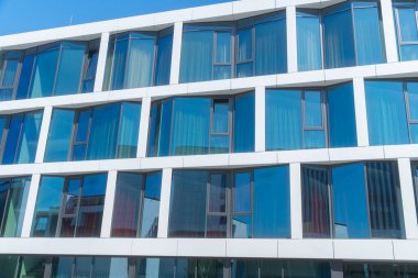 Geometrik desenli modern cam bina mavi gökyüzünü yansıtır. Temiz çizgiler, simetri ve çağdaş mimari parlak bir şehir manzarası oluşturur.