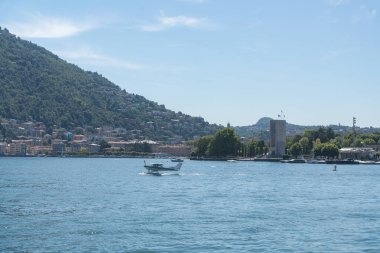 Dağlarla çevrili sakin bir göl ve göl kenarı köyü boyunca küçük bir tekne hareket eder. Yumuşak ışık ve açık alanla dolu sakin bir yaz sahnesi. İtalya, Como