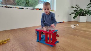 Genç bir çocuk renkli ahşap bir blok yapısını ahşap bir zemine itiyor. Basit bir iç mekan sahnesi eğlenceli keşifler, koordinasyon ve erken yaratıcı gelişimi vurgular