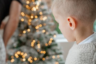 Yumuşak, sıcak bir sahne, parlayan Noel ağacı ışıklarını izleyen bir çocuk. Bulanık festival arka planı mevsimlik ve aile tasvirleri için mükemmel büyülü bir tatil havası yaratır.