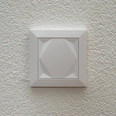 Dokulu alçı bir yüzeye monte edilmiş modern beyaz bir duvar anahtarının minimal yakın çekimi. Temiz çizgiler, nötr tonlar ve basit geometrik tasarım ev içi temalar için uygun hale getirir