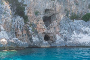 Güneşli bir günde parlak turkuaz suyun üzerinde yükselen sarp kayalıklar. Doğal dokular, mavi tonlar ve el değmemiş bir manzara seyahat temaları için mükemmel bir kıyı manzarası yaratır. İtalya