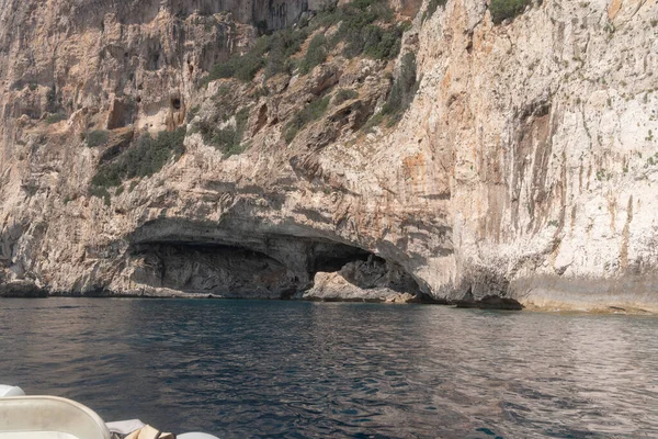 Sakin mavi suyun üzerinde kayalık deniz mağarası açılıyor. Doğal dokular, güneş ışığı ve kıyı oluşumları Akdeniz kıyıları ve tekne gezileri için tipik dramatik bir unsur oluşturur..