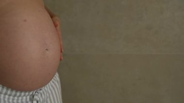 Hamile kadın karnına hafifçe dokunuyor. Doğmamış bebekle duygusal bağ kurma anı, annelik ve hamilelikle ilgili doğal yaşam tarzı fotoğrafı.