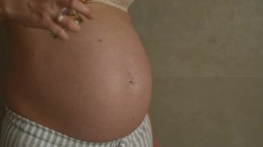 Hamile bir kadının vücut yağı sürerken ve karnını nazikçe ovalarken. Hamilelik sırasında cilt bakımı, vücut bakımı, annelik, doğum öncesi sağlık ve kendine bakım kavramı