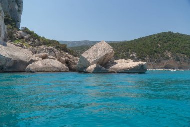 Doğal bir kıyı şeridi boyunca berrak turkuaz sudan yükselen etkileyici kayalık oluşumlar. Güneşli hava ve el değmemiş manzara dingin ve manzaralı bir açık hava gezisi manzarası yaratır. İtalya, Sardunya