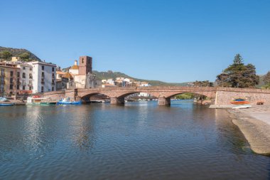 Suda yansımaları olan sakin bir nehri geçen tarihi bir taş köprü. Yumuşak gün ışığı ve doğal çevre huzurlu bir seyahat ve manzara yaratıyor, Bosa, Italien