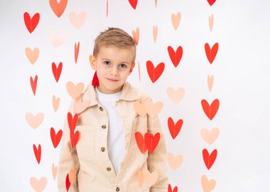 Beyaz arka planda asılı kırmızı kalplerle çevrili şirin çocuk portresi. Aşk, şefkat, çocukluk masumiyeti.
