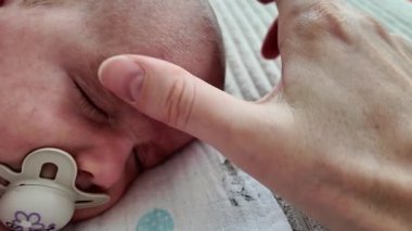 Annenin bebek kaşlarına nazikçe yağ sürdüğü ve iki gözünün arasına masaj yaptığı aşırı yakın çekim. Bebek bakımı, bağlanma, hassasiyet ve doğal cilt bakımı kavramı.