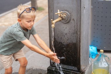 Sokakta halka açık bir çeşmede ellerini durulayan bir çocuk. Seyahat yaşam tarzı, hijyen ve kentsel çocukluk anı