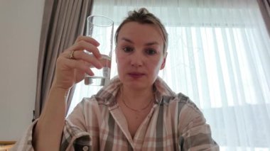 İçerideki kız bir bardak suyu bitiriyor. Günlük susuzluk rutini ve evde kendine bakmanın sembolü.