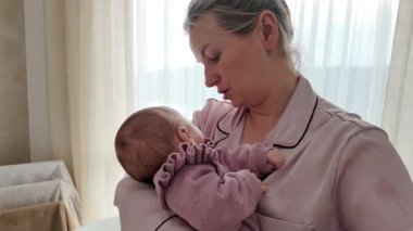 Genç anne yeni doğmuş bebeğini kucağında tutuyor ve evde usulca ninni söylüyor. Hassas bağ anı, erken annelik ve duygusal bağ konsepti..