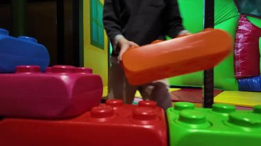 Çocuk, kapalı bir oyun alanında büyük yumuşak köpük bloklarıyla oynuyor. Aktif oyun ortamı hareketle fiziksel gelişimi, koordinasyonu ve eğlenceli öğrenmeyi teşvik eder