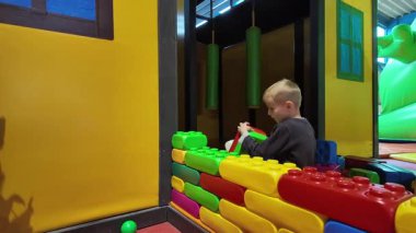 Çocuk kapalı bir oyun bahçesinde renkli yumuşak bloklar yığıyor. Yaratıcı oyun hayal gücünü, iyi motor becerileri ve güvenli bir oyun ortamında erken öğrenmeyi destekler.