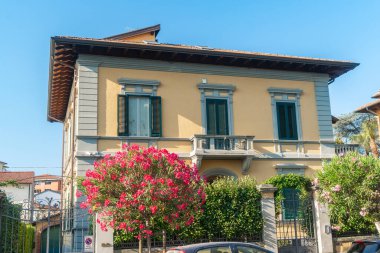 İtalyan evi cephesi çiçek açan pembe çiçekler ve yeşil panjurlarla süslenmiş. Parlak yaz günü ve Akdeniz yaşam tarzı atmosferi.