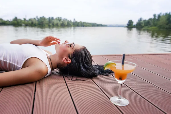 Girl lying on the dock, standing next to a cocktail Royalty Free Stock Images